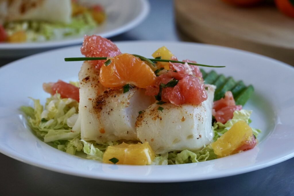 A dinner plate with the baked cod topped with the tangy citrus salad.