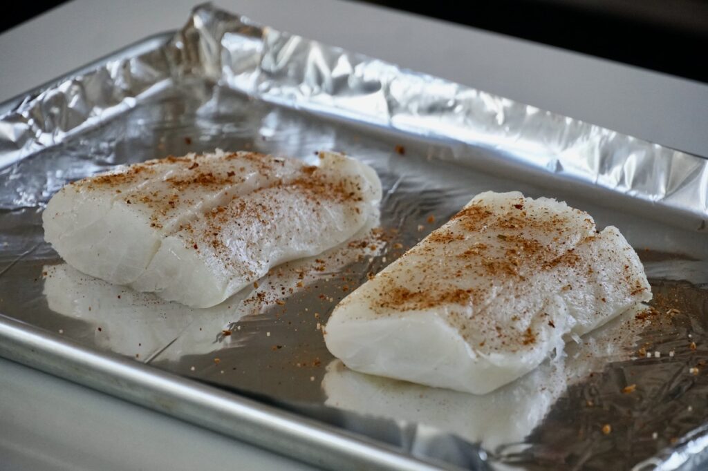 Two fillets of fresh cod rubbed with oil and sprinkled with seasoning.