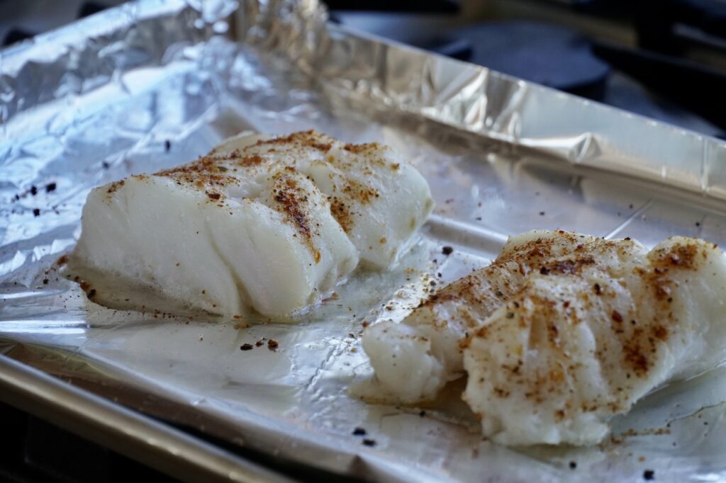 Two pieces of oven-baked cod on a foil-lined baking tray.