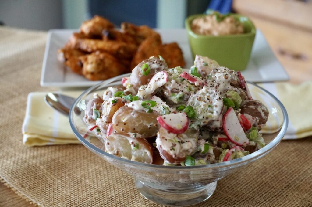 A bowl of Warm Potato Salad served with chicken wings.