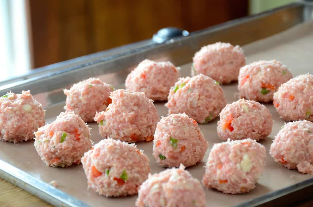 The meatballs rolled out onto a parchment-lined baking sheet ready to be baked.