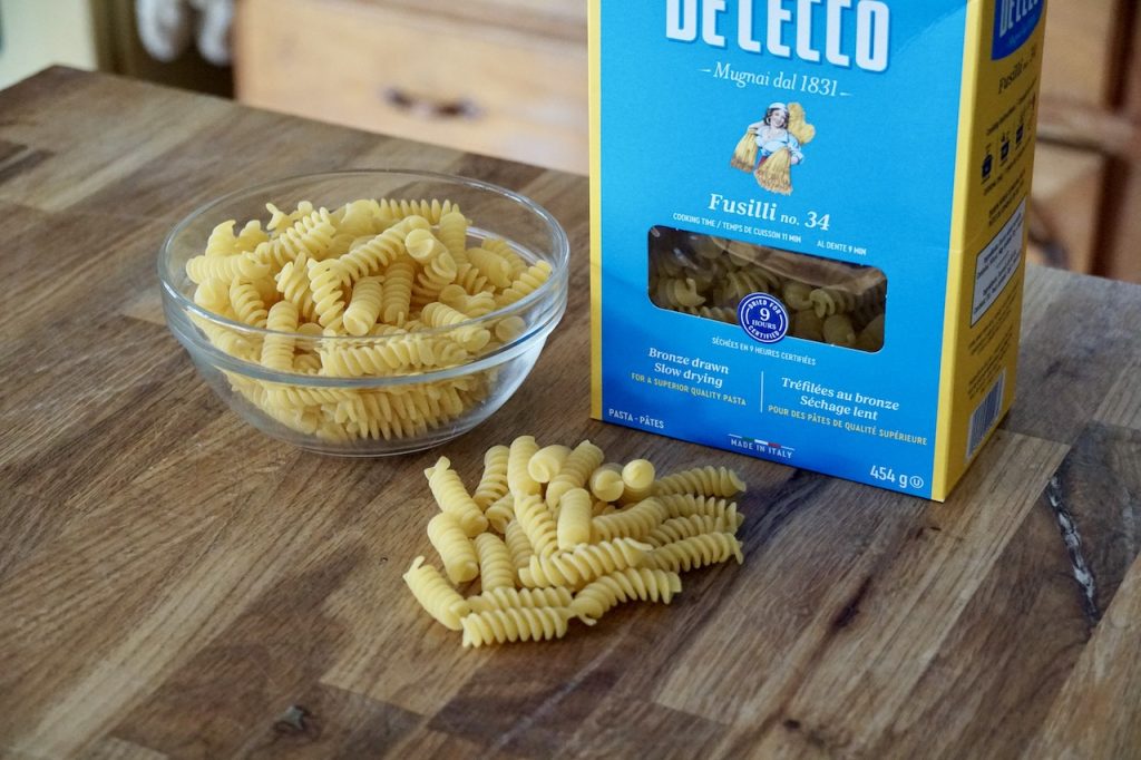 A box of fusilli pasta and a bowl containing short noodles.