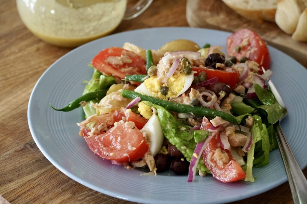 TUNA SALAD NIÇOISE tossed in a large bowl then served to luncheon plates.