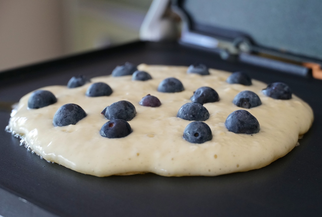 The batter sizzling on a hot griddle dotted with fresh, wild blueberries