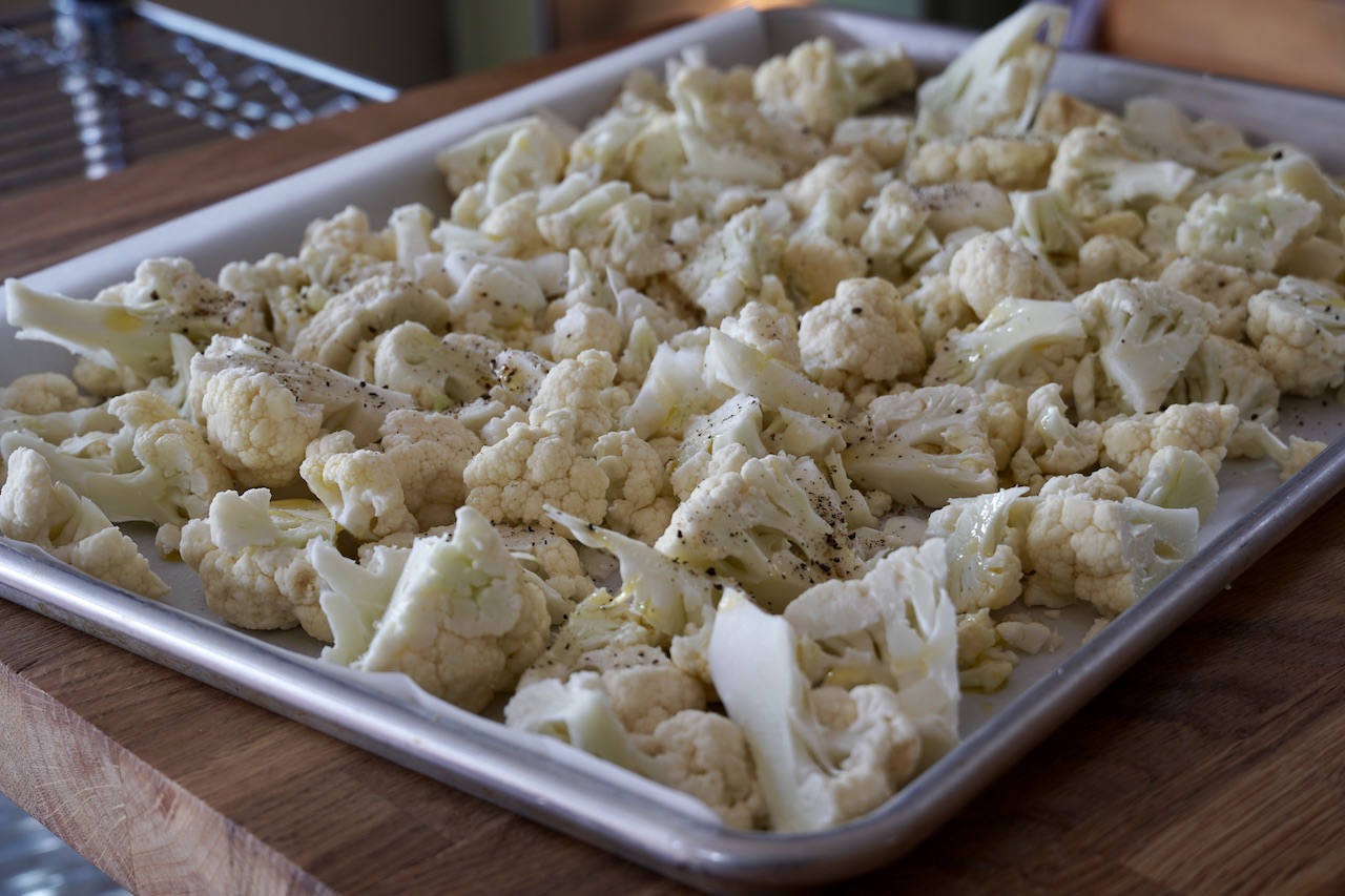 A baking sheet filled with chopped cauliflower, ready for the oven