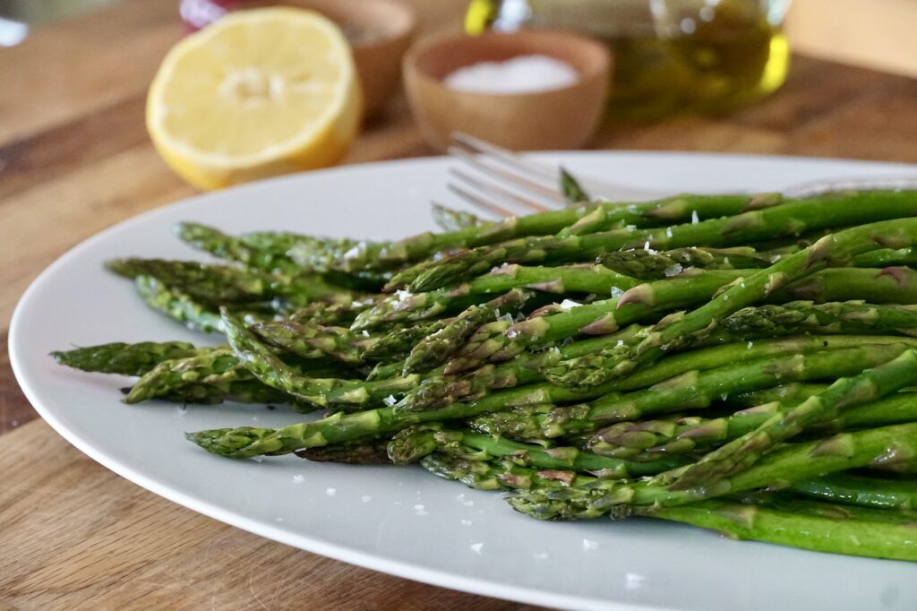 Oven-roasted asparagus served on an oval platter with a lemon wedge served on the side.