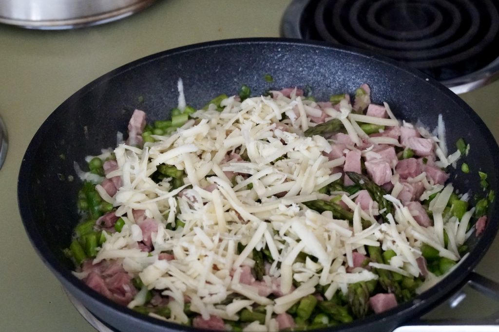 The ham and veggies sauteed in a skillet, sprinkled with cheese