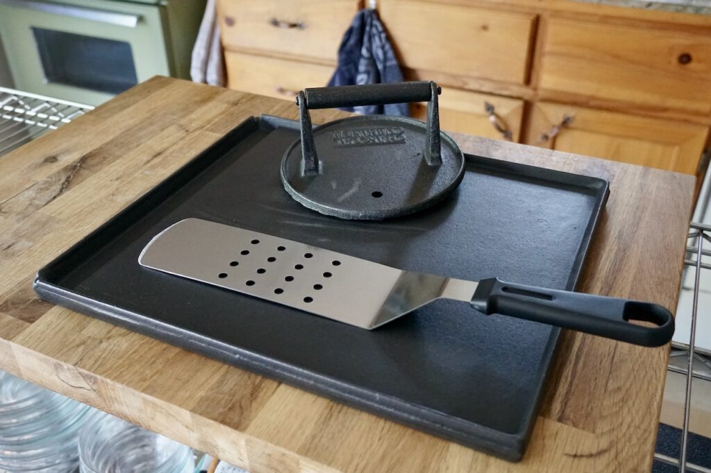 A flat cast-iron griddle, a burger press and a stainless flipper.