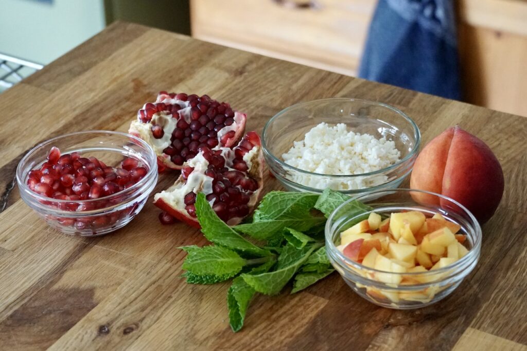 The toppings for the salad include feta cheese, chopped fresh herbs and either pomegranate seeds or diced peaches