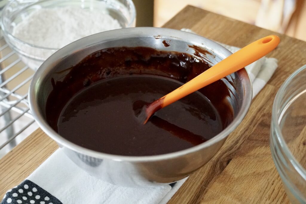 A bowl containing the melted butter, chocolate, cocoa powder and vanilla.