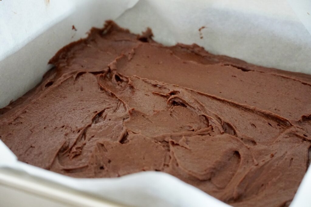 The parchment-lined baking pan filled with the dense brownie batter