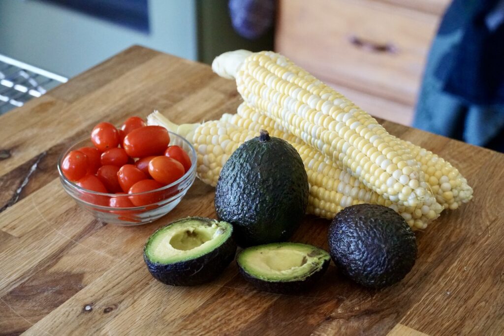 Halved avocados, cobs of corn and cherry tomatoes.