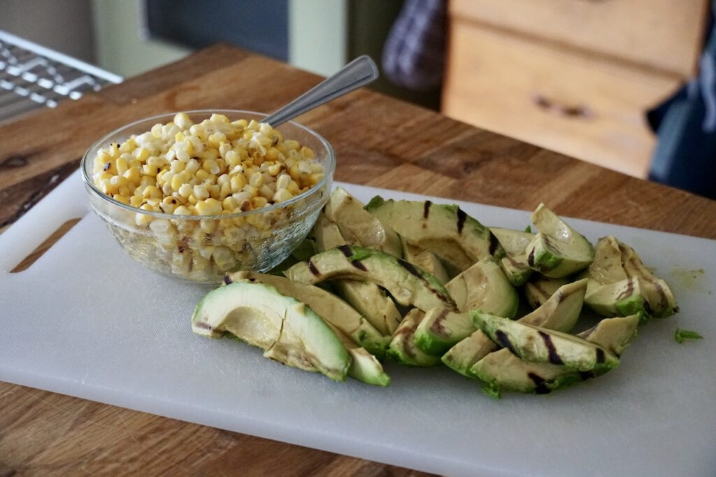 Sliced grilled avocado and kernels of corn ready to be added to the tops of the salads.

