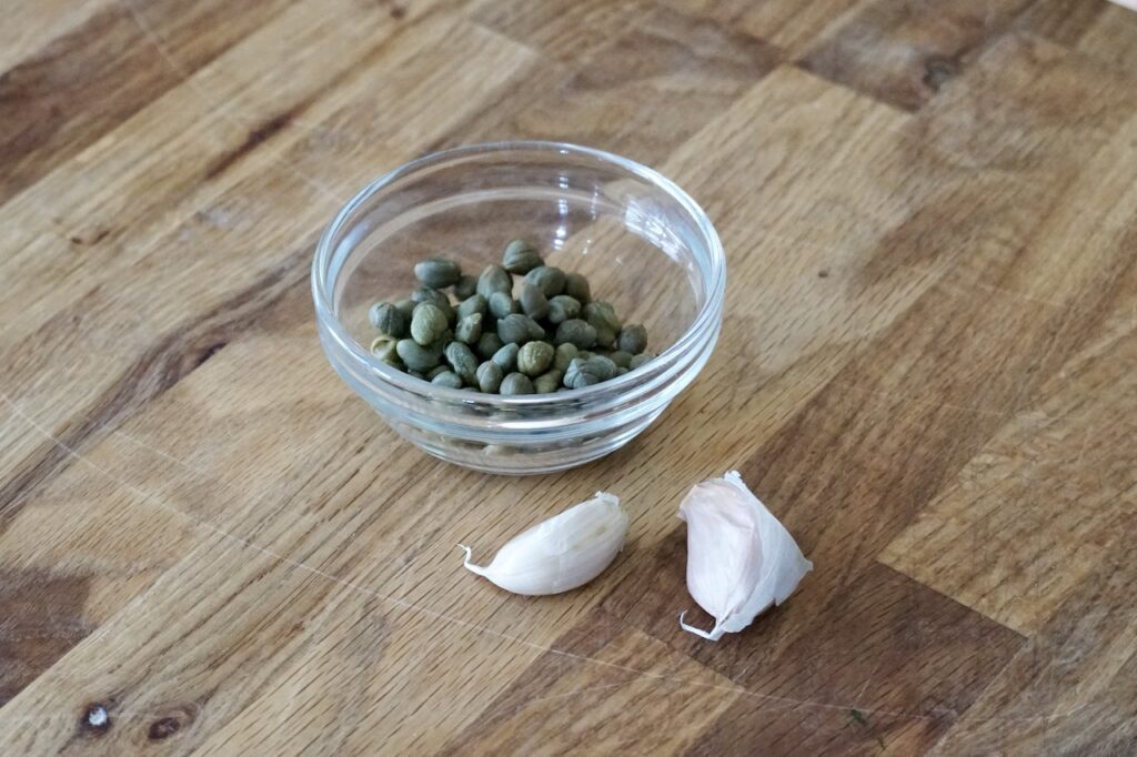 A bowl of capers and two cloves of garlic