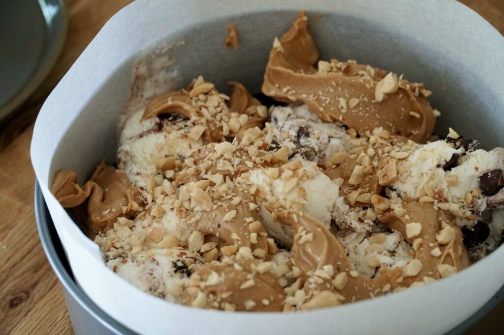 The ice cream, peanut butter and chopped nuts spooned into the lined springform pan