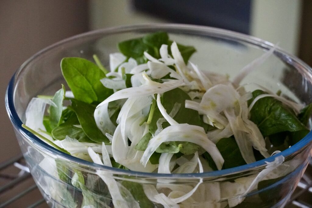 The baby spinach and shaved fennel tossed up in a large salad bowl.
