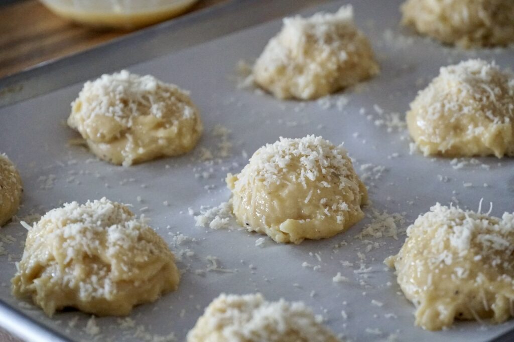 Pipe or scoop portions of the dough onto baking sheets and finish with a brush of egg wash and a sprinkle of Parmesan.