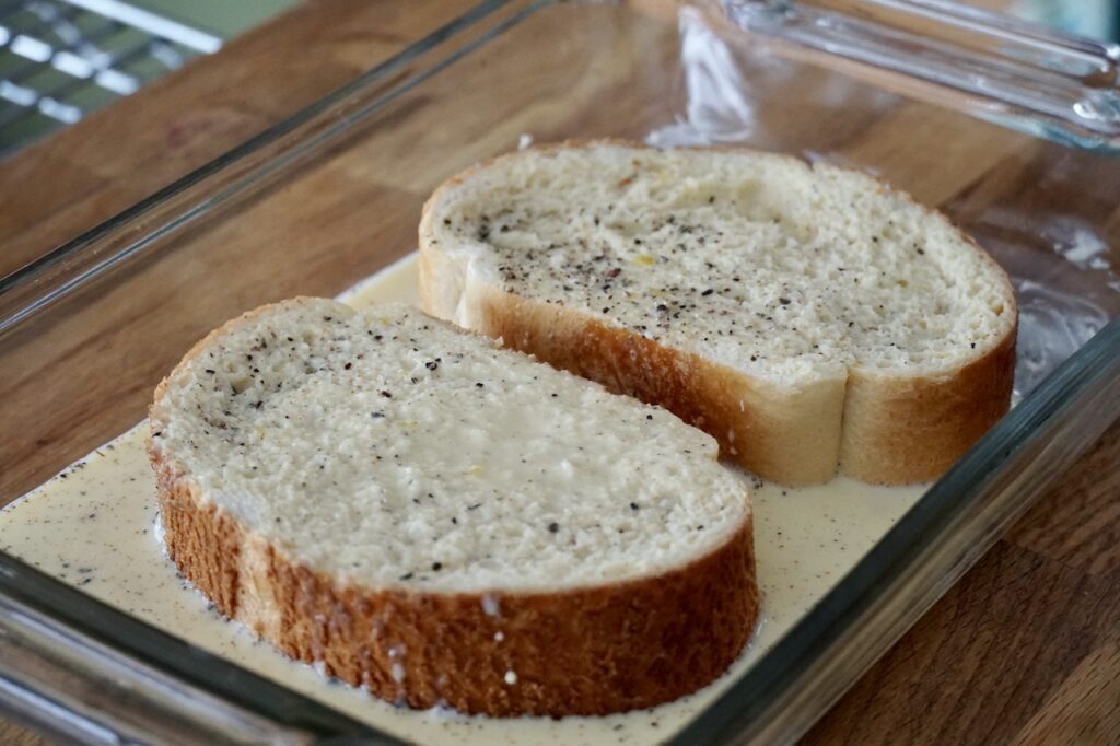 Two thick slices of bread soaking up the seasoned egg and milk batter.