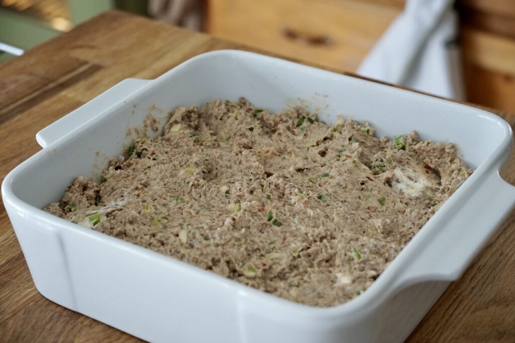 The cream cheese, veggie and beef mixture spread out in a square casserole dish.