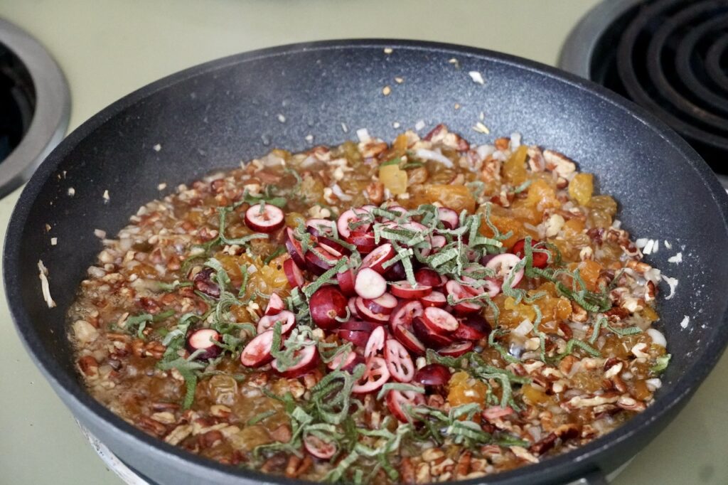 A skillet with the fresh and dried fruit and nuts being sautéed in butter