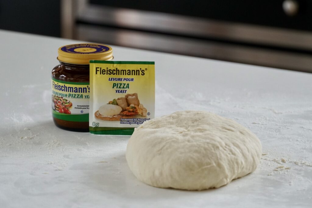 A ball of homemade pizza dough and a package and bottle of Fleischmann's Pizza Yeast.