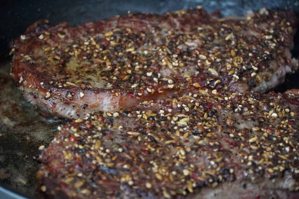 Close up of the fragrant seasoning clinging to the seared, browned steaks.