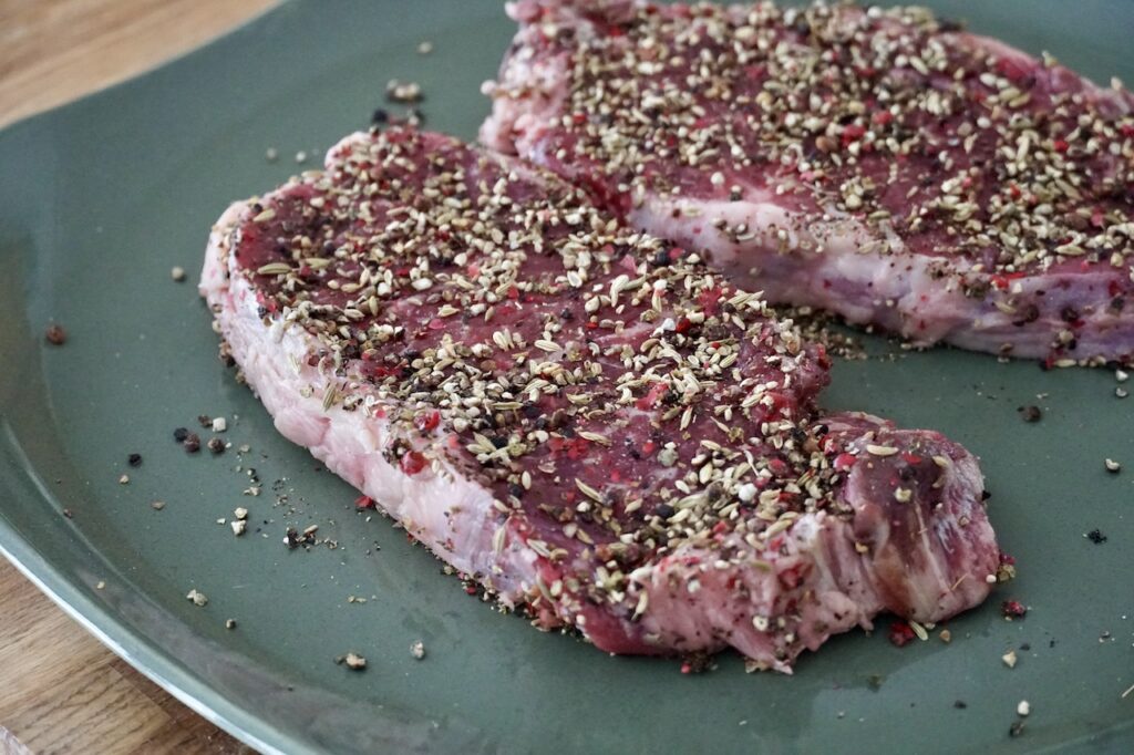 Two sirloin steaks seasoned with crushed peppercorns and fennel seeds.