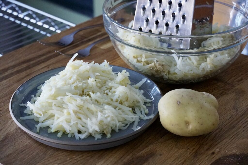 The par-boiled Yukon gold potatoes grated sing a box grater.