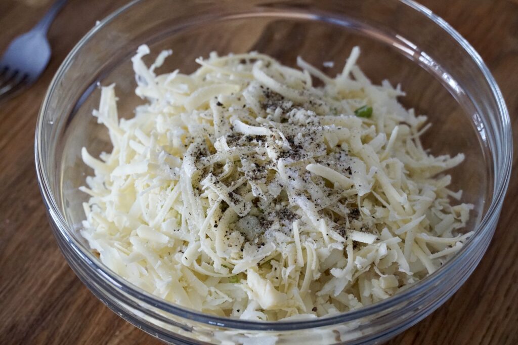 Shredded par-boiled potatoes tossed in a bowl with green onion and Gruyere.