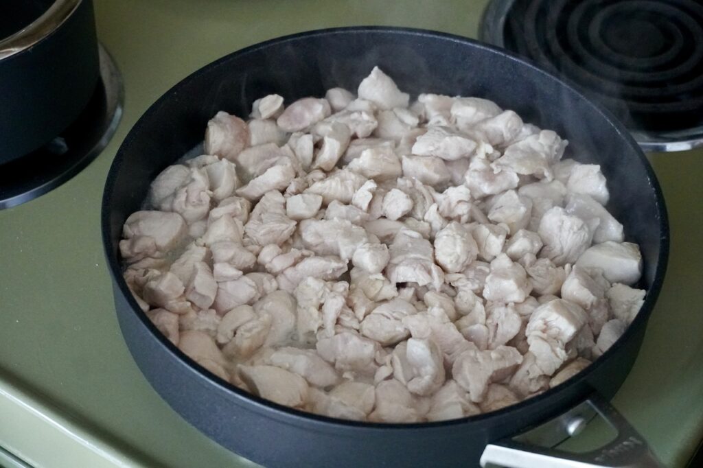 A large, deep skillet filled with seared morsels of chicken.