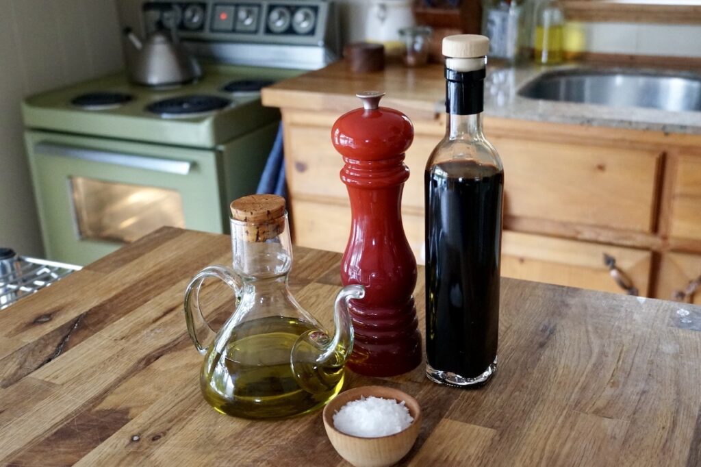 Bottles of premium balsamic vinegar and olive oil with bowls of sea salt flakes and freshly cracked black pepper.