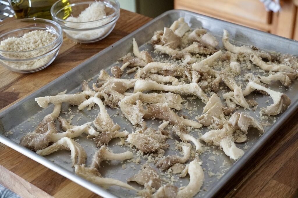 The breaded oyster mushrooms spread out on a large baking sheet.