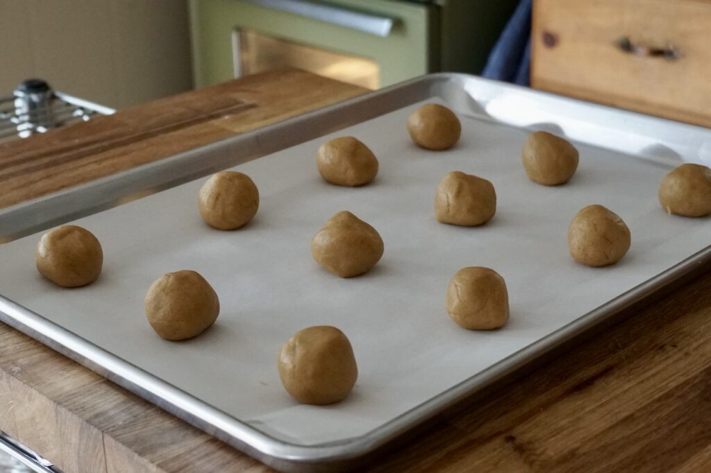 A cookie sheets with twelve peanut butter cookie dough balls.