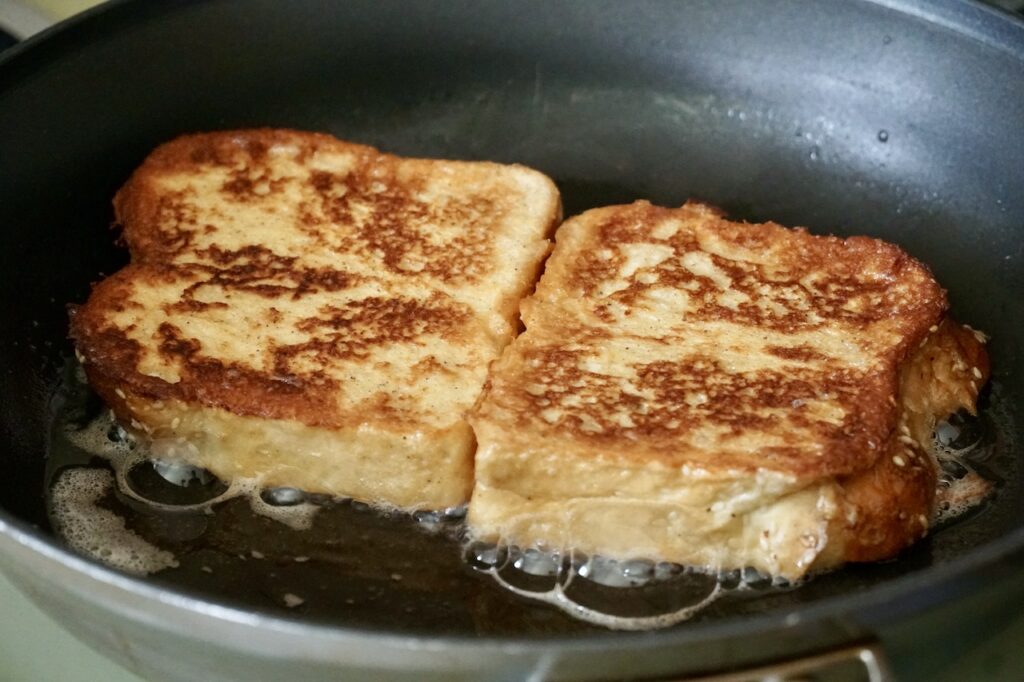 Two slices of bread cooking in a non-stick skillet.