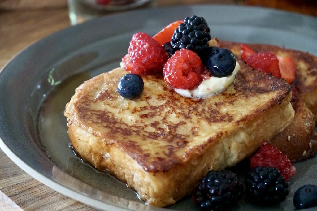 A place of the french toast topped with butter, berries and maple syrup.