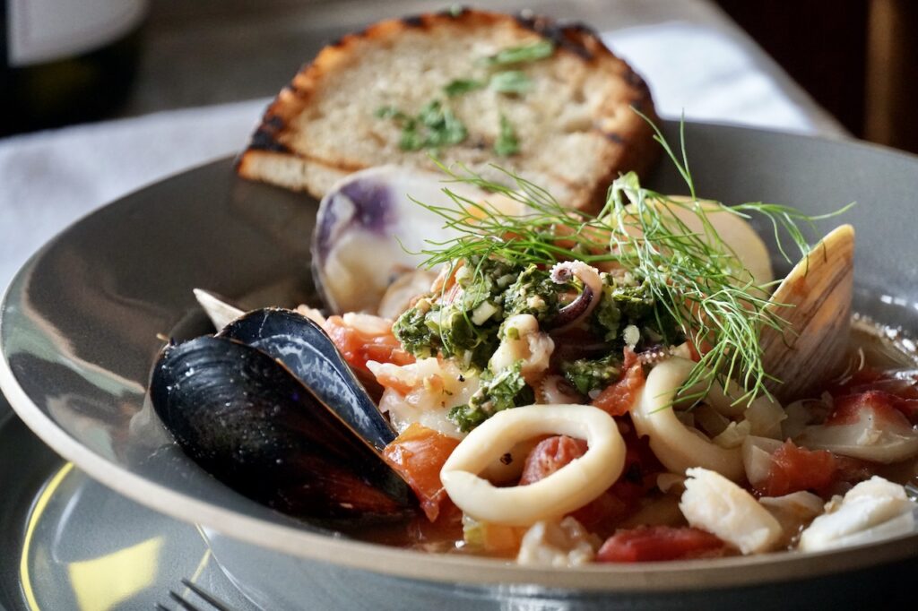 A close up of the morsels of fresh seafood and shellfish in a soup plate.