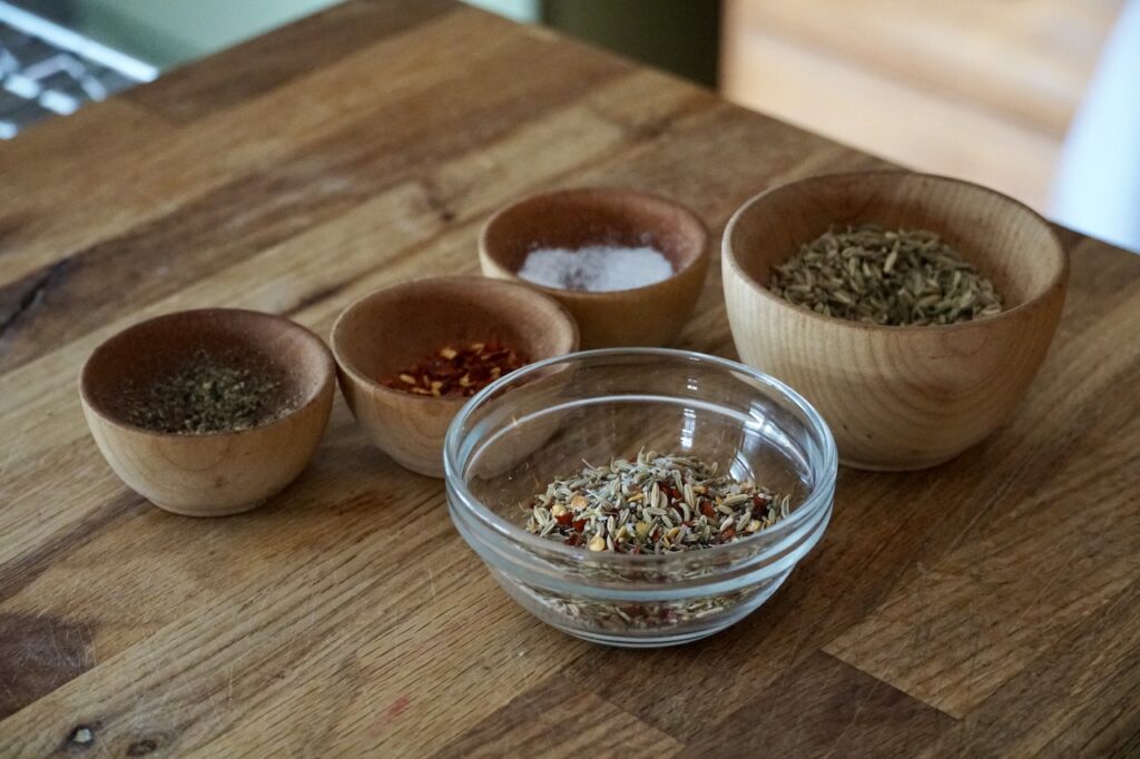 A bowl containing fennel seeds, chili flakes, kosher salt and black pepper.