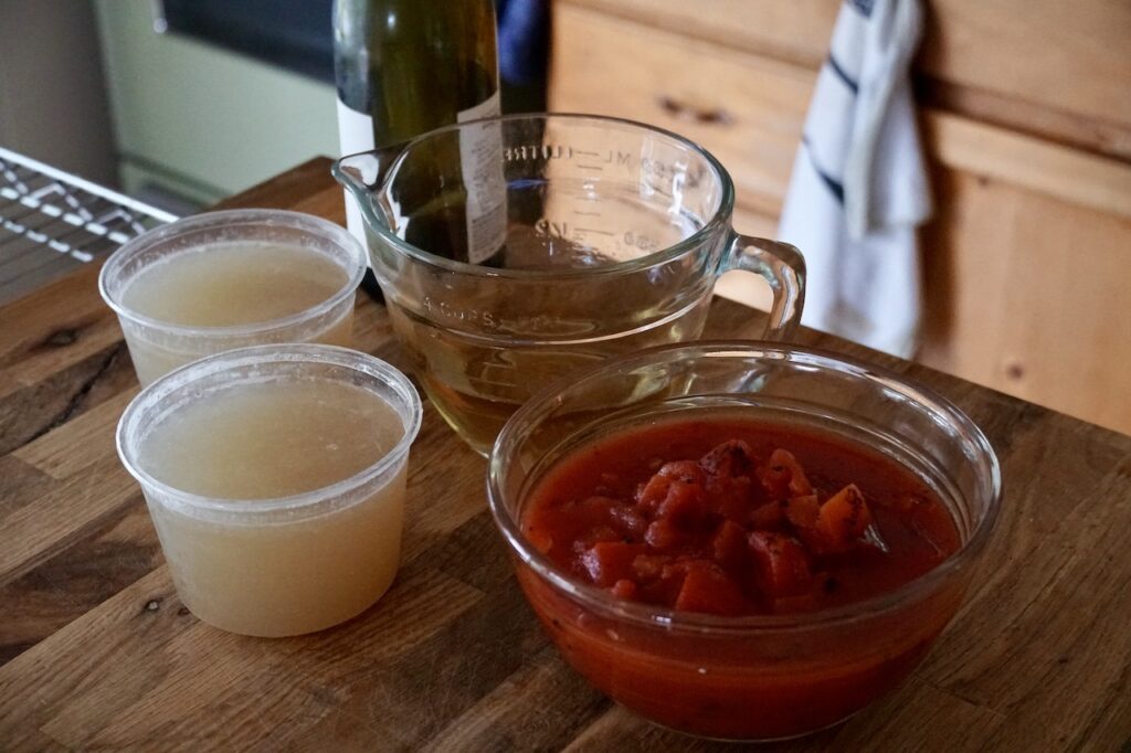 Containers of fish stock, a measure of dry white wine and a bowl of diced tomatoes.