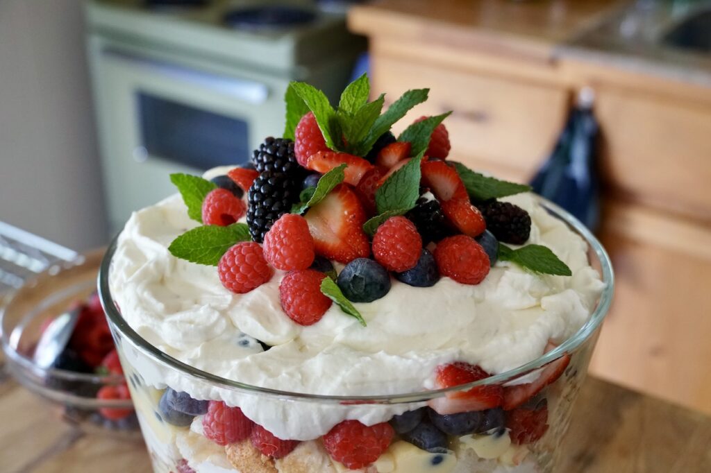 A bowl of homemade trifle garnished with fresh berries and mint leaves.