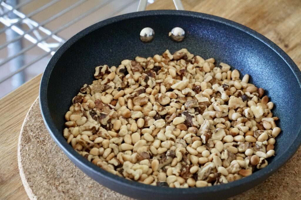A skillet containing toasted pine nuts and walnuts.