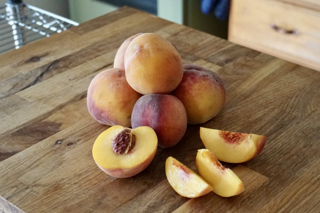 A grouping of fresh peaches, one of which is cut open and sliced.