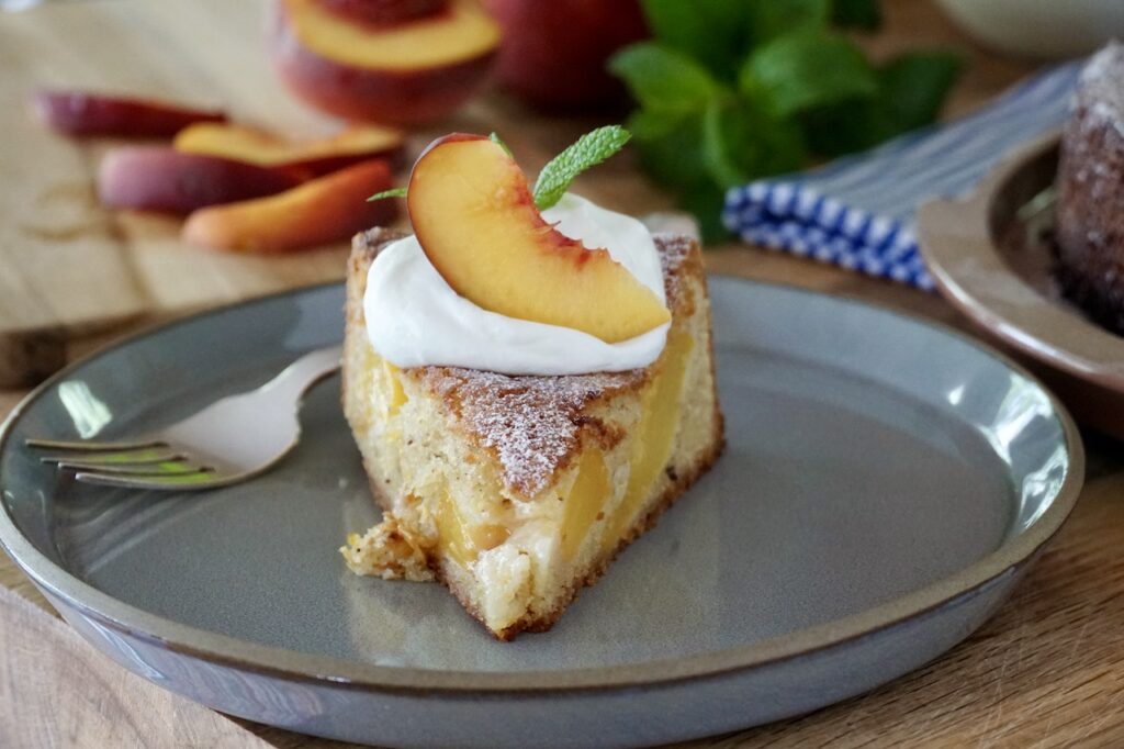 The slice of fresh Peach Cake topped with whipped cream, mint and a peach slice.