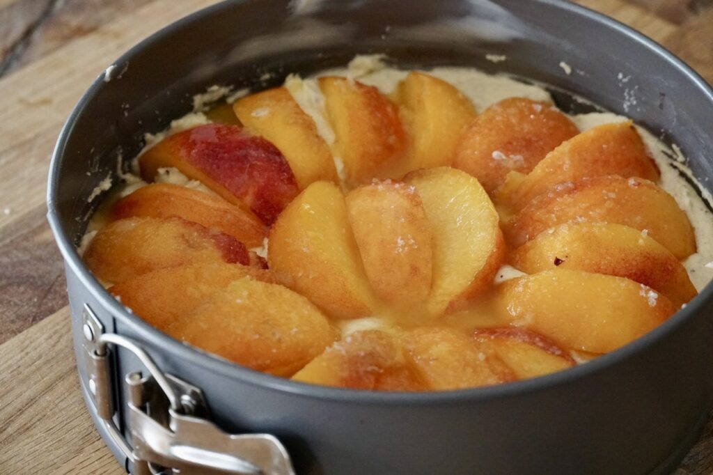 The cake batter is transferred into a spring-form pan then, topped with the sliced peaches.