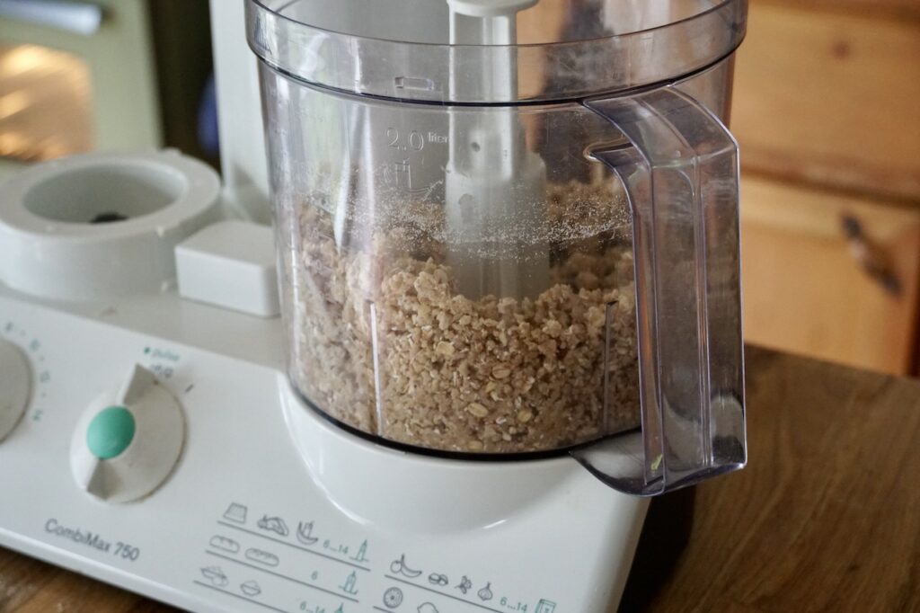 The canister of the food processor filled with the course meal for the shortbread base.