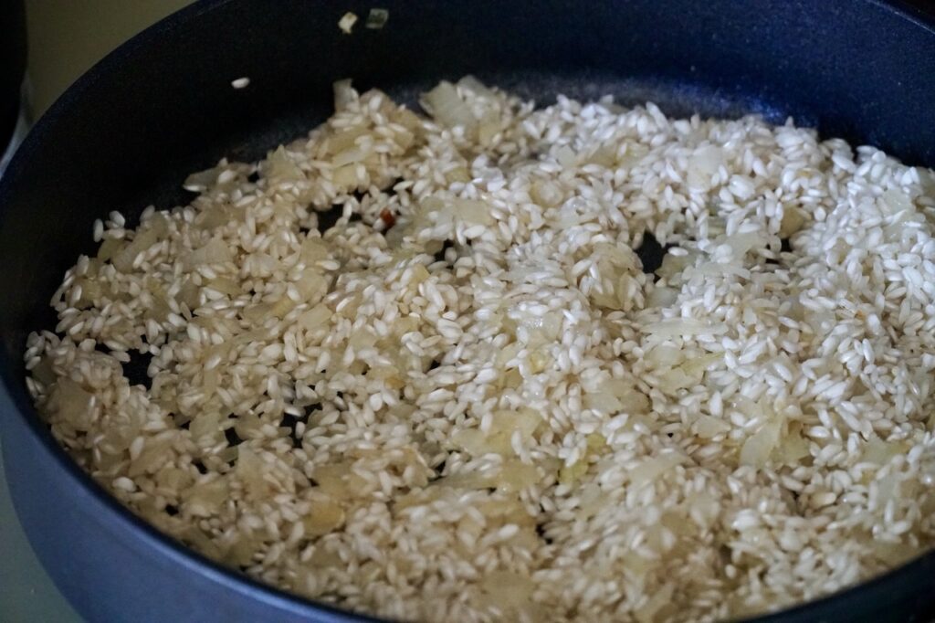 A skillet with the onions and carnaroli rice cooking in butter and olive oil.