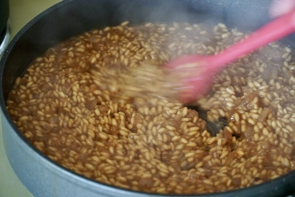 The pot being stirred slowly so that the rice soaks up the liquids.