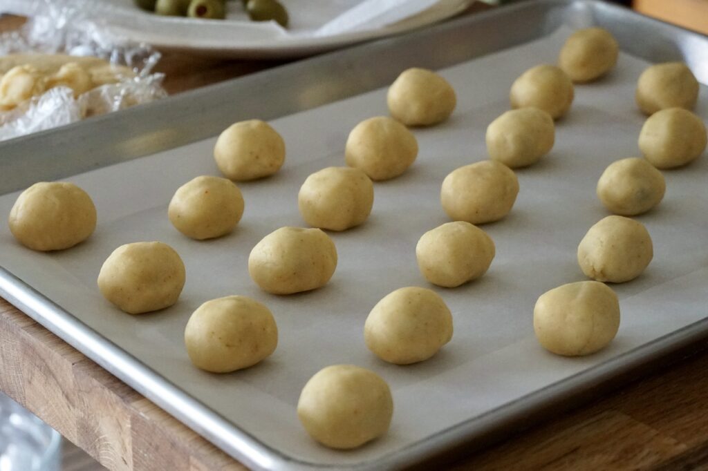 Baked Cheddar Olives shaped and positioned on a parchment-lined baking sheet.