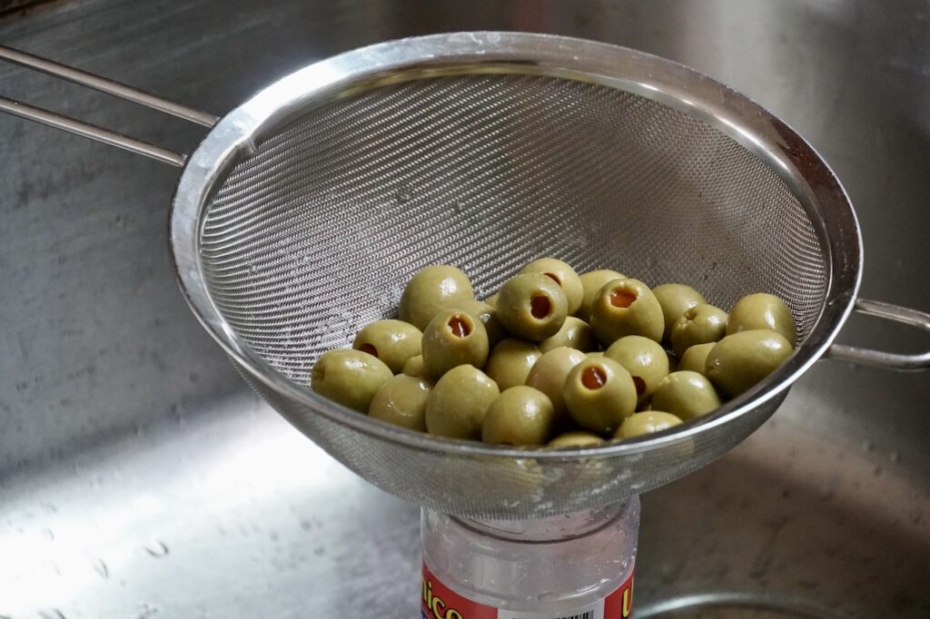 Pimento-stuffed olives straining in a stainless sieve.