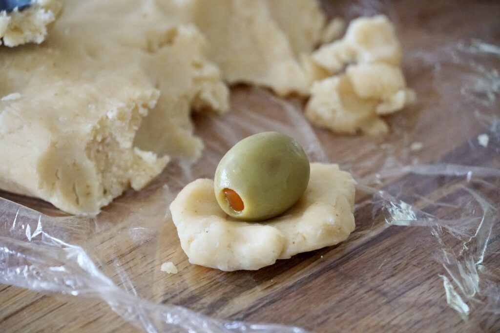 One pimento-stuffed green olive resting on a small circle of cheddar pastry dough.