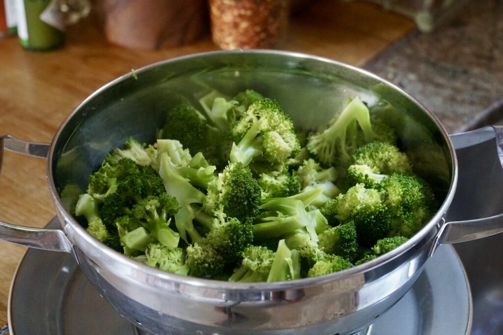 Steamed broccoli cooling in a stainless colander.